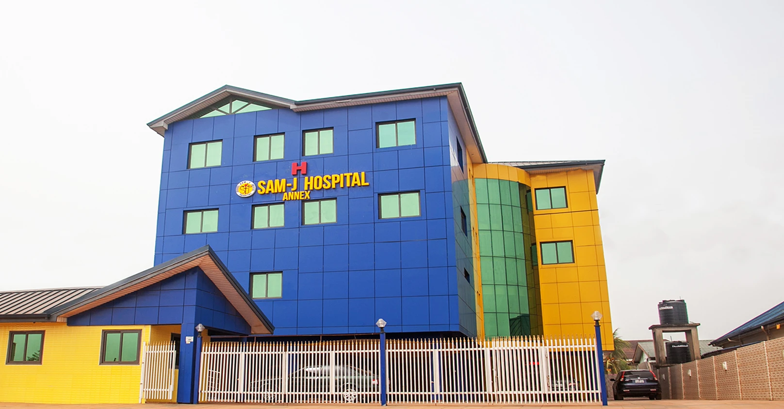 The blue and yellow SamJ Hospital building in Haatso